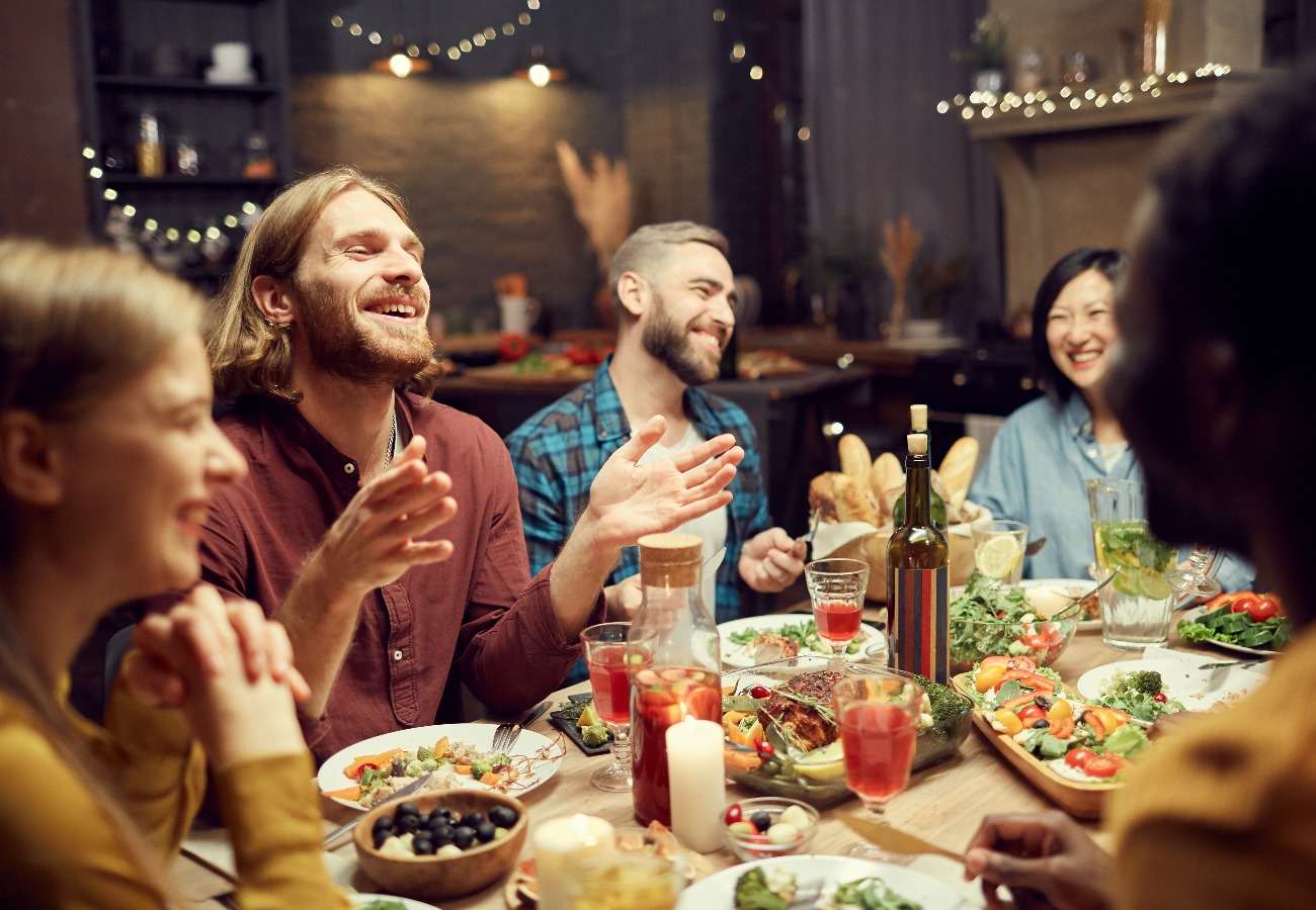 Group of emotional young people enjoying dinner party with friends and smiling happily sitting at table in dimly lit room, copy space